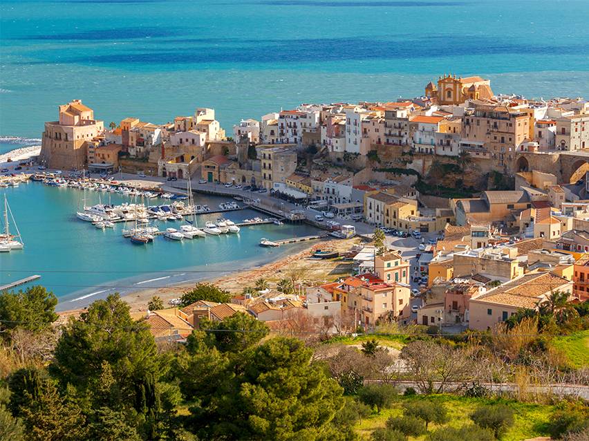 Ville côtière avec des maisons colorées, un port rempli de bateaux et la mer azur.