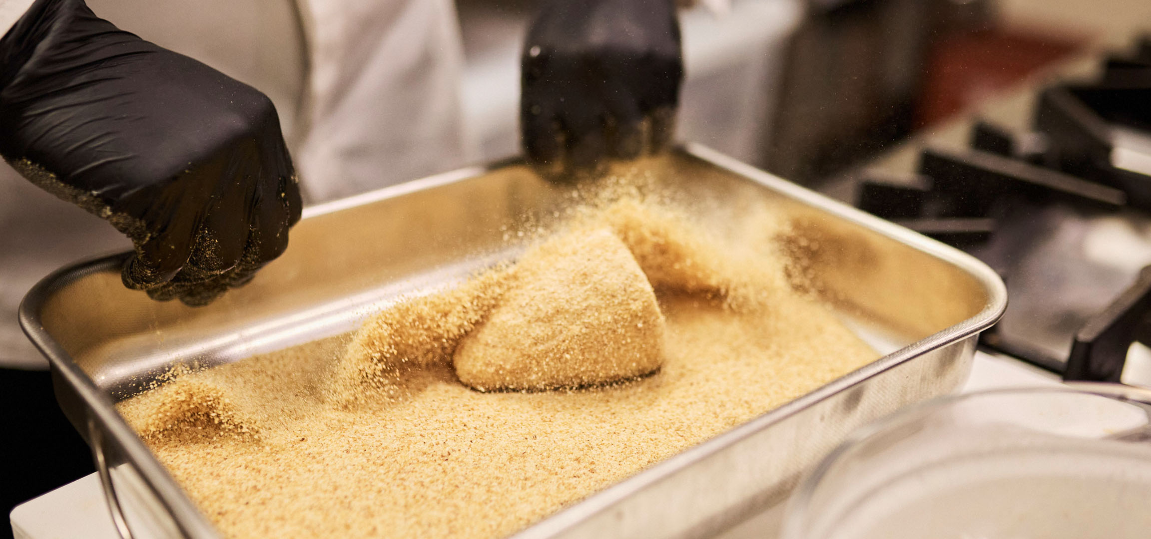 Un chef pane des aliments dans de la chapelure dans un plat en métal.