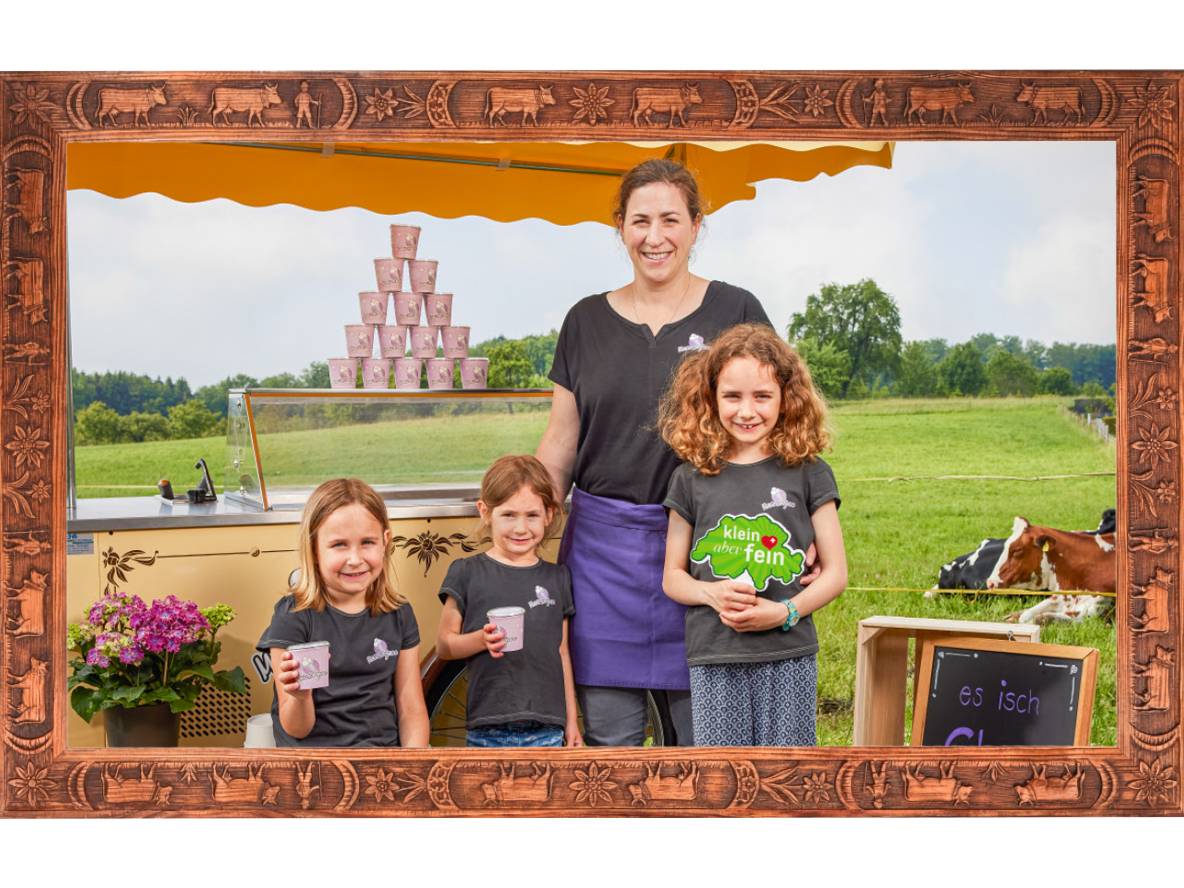 Famiglia vende coppe gelato da un carretto in un prato verde con mucche.