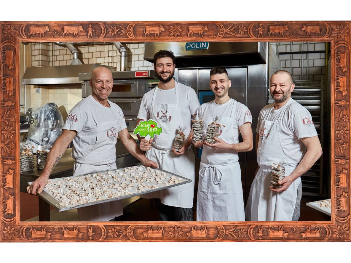 Quattro fornai in cucina presentano prodotti da forno e biscotti confezionati, incorniciati in legno.