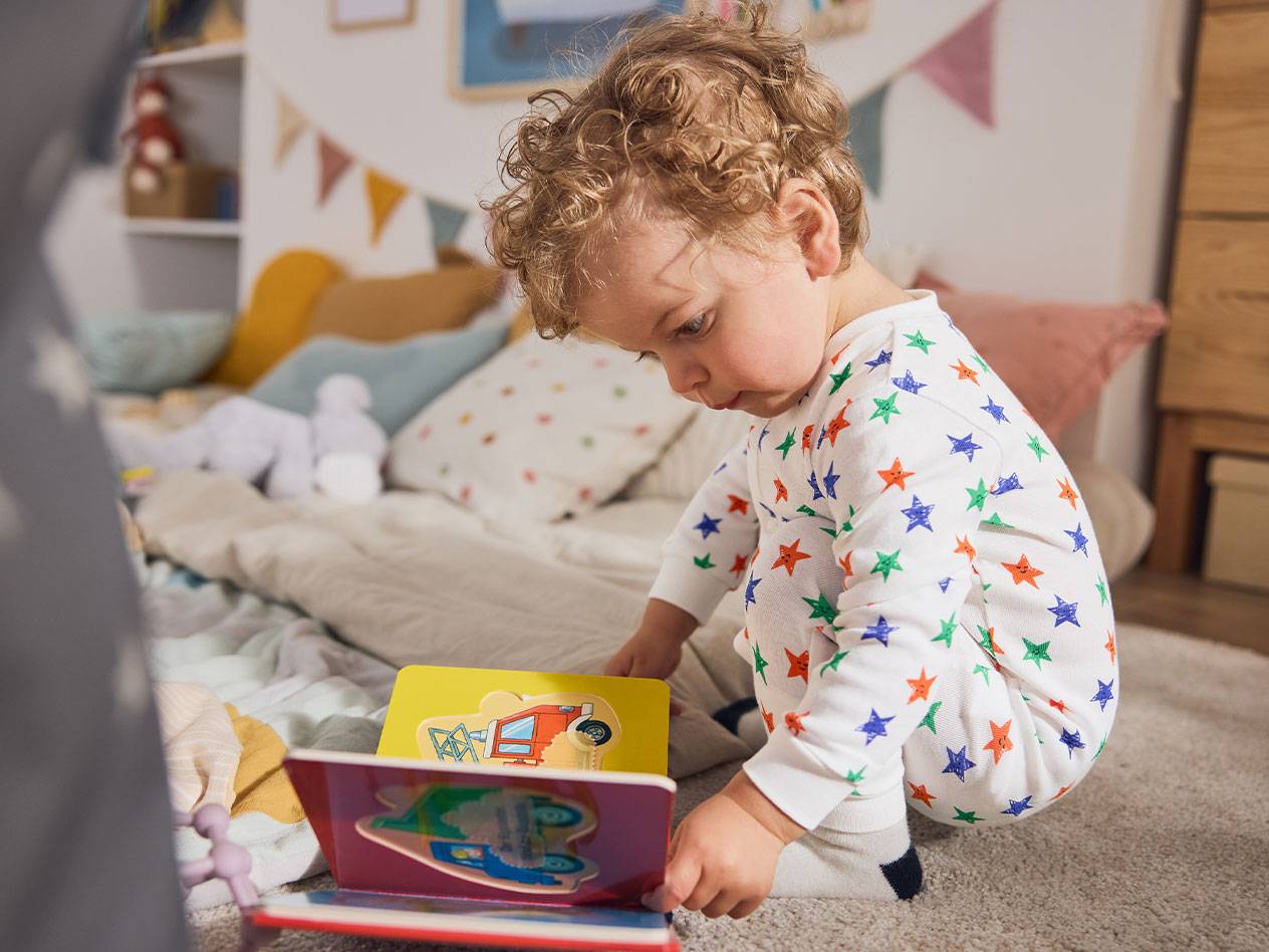 Un tout-petit en pyjama étoilé, assis sur le tapis, lisant un livre.