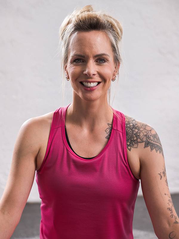 Une femme souriante en débardeur de sport rose avec des tatouages à l'épaule.