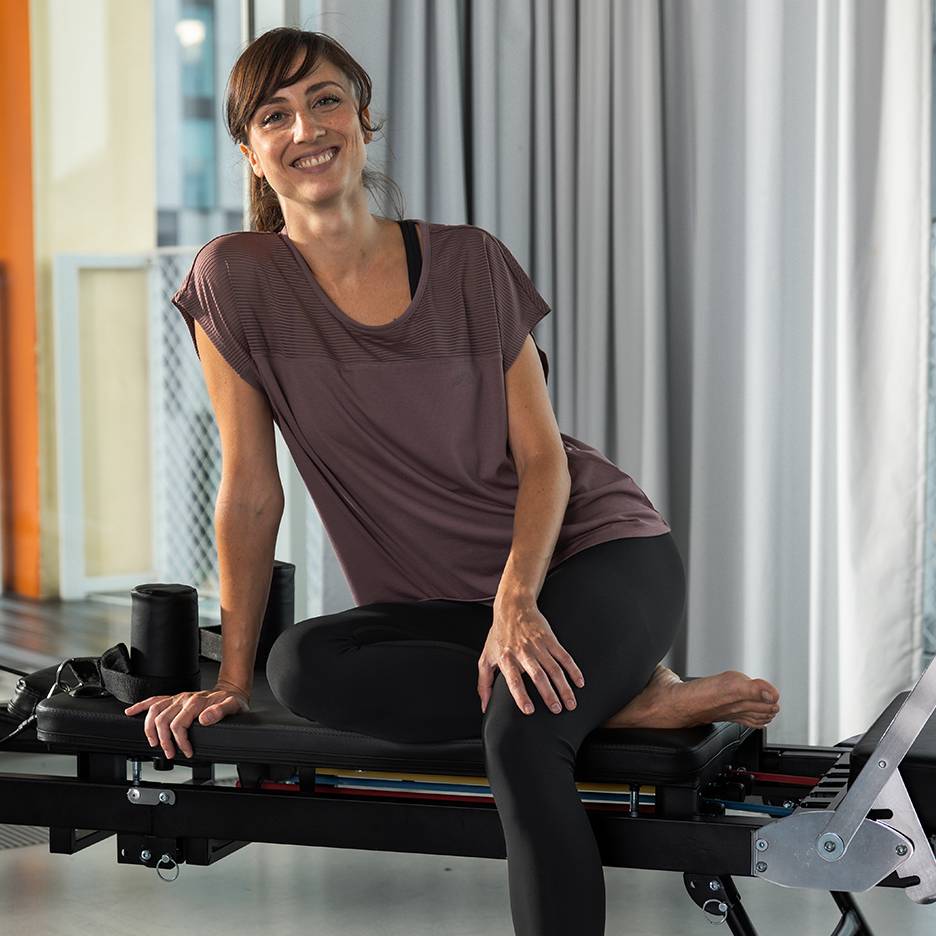 Donna in abbigliamento sportivo sorridente, seduta su una macchina Pilates.