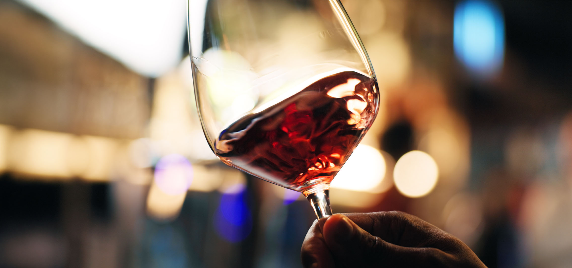 Nahaufnahme eines Glases Rotwein mit verschwommenen Lichtern im Hintergrund.