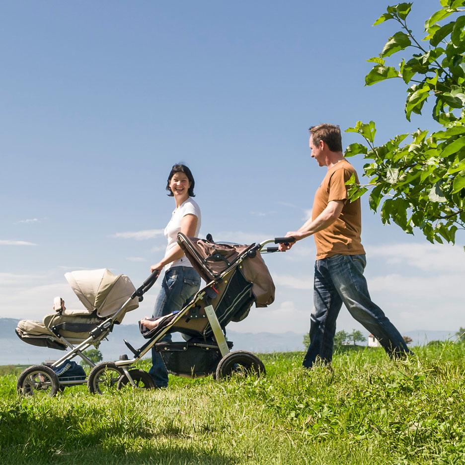 Eine Familie spaziert mit einem Kinderwagen über eine Wiese.