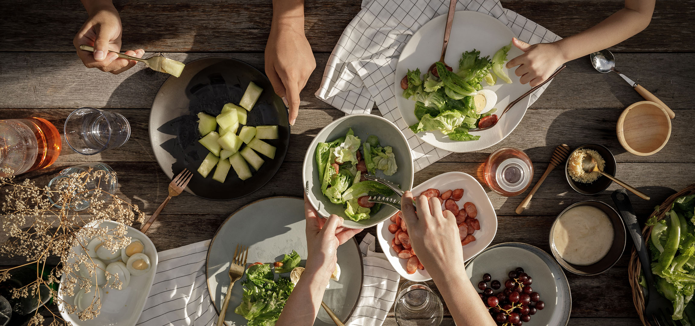 Draufsicht auf einen Tisch mit Salat, Würstchen und Melone, Personen servieren Essen.