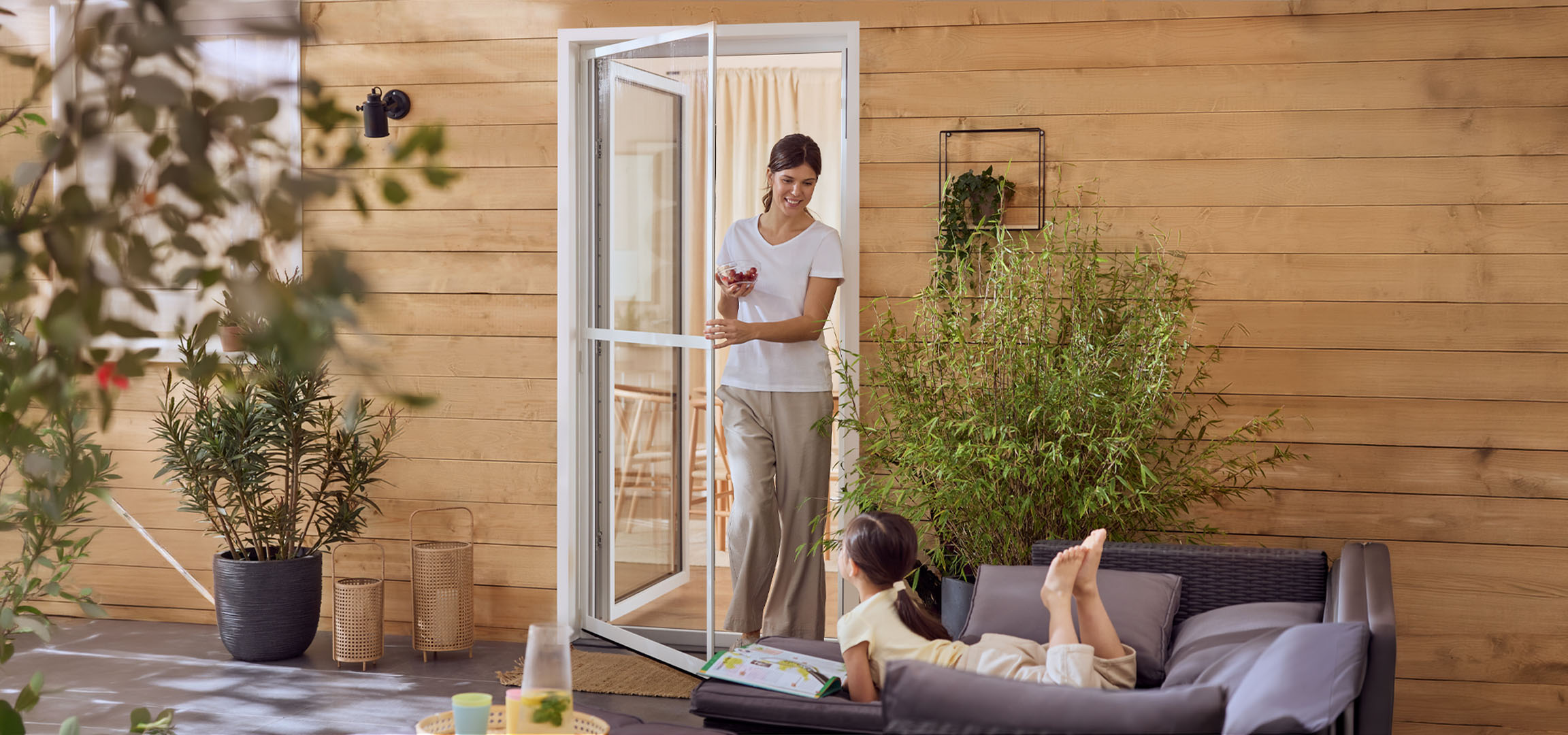 Frau und Mädchen genießen eine Terrasse mit Gartenmöbeln und Pflanzen.