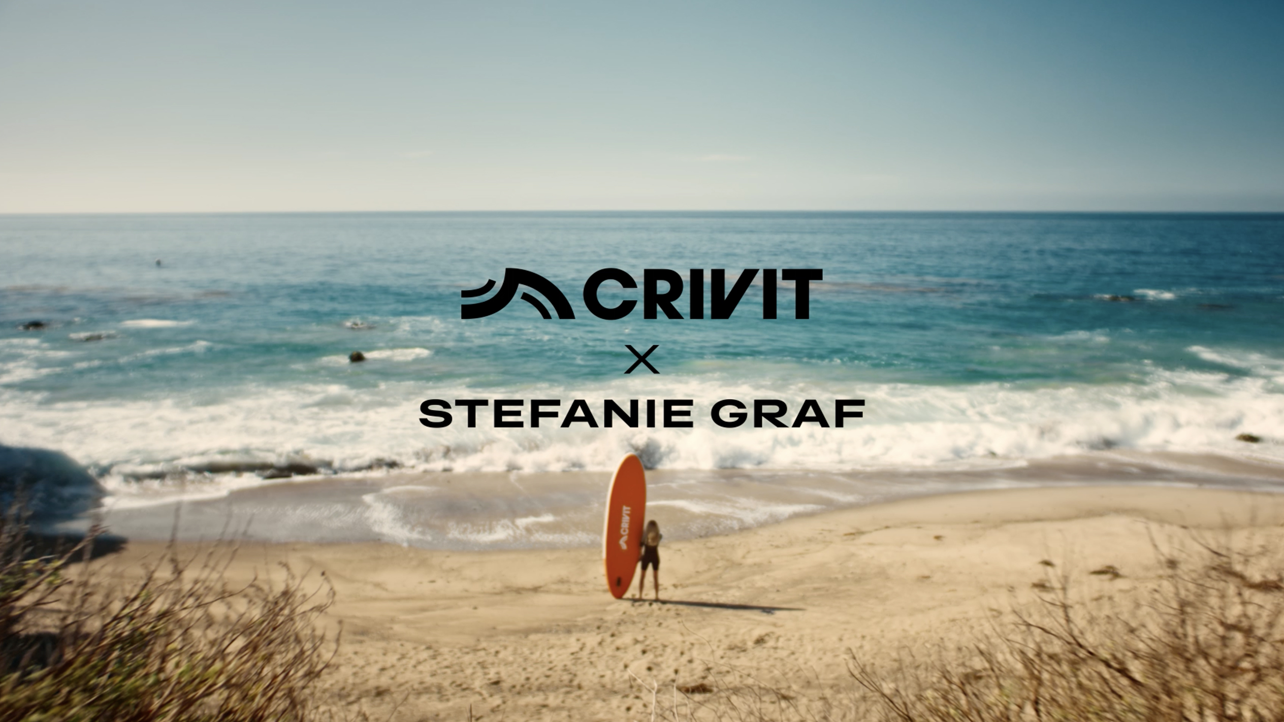Femme avec une planche de SUP orange sur une plage de sable, avec la mer en arrière-plan.