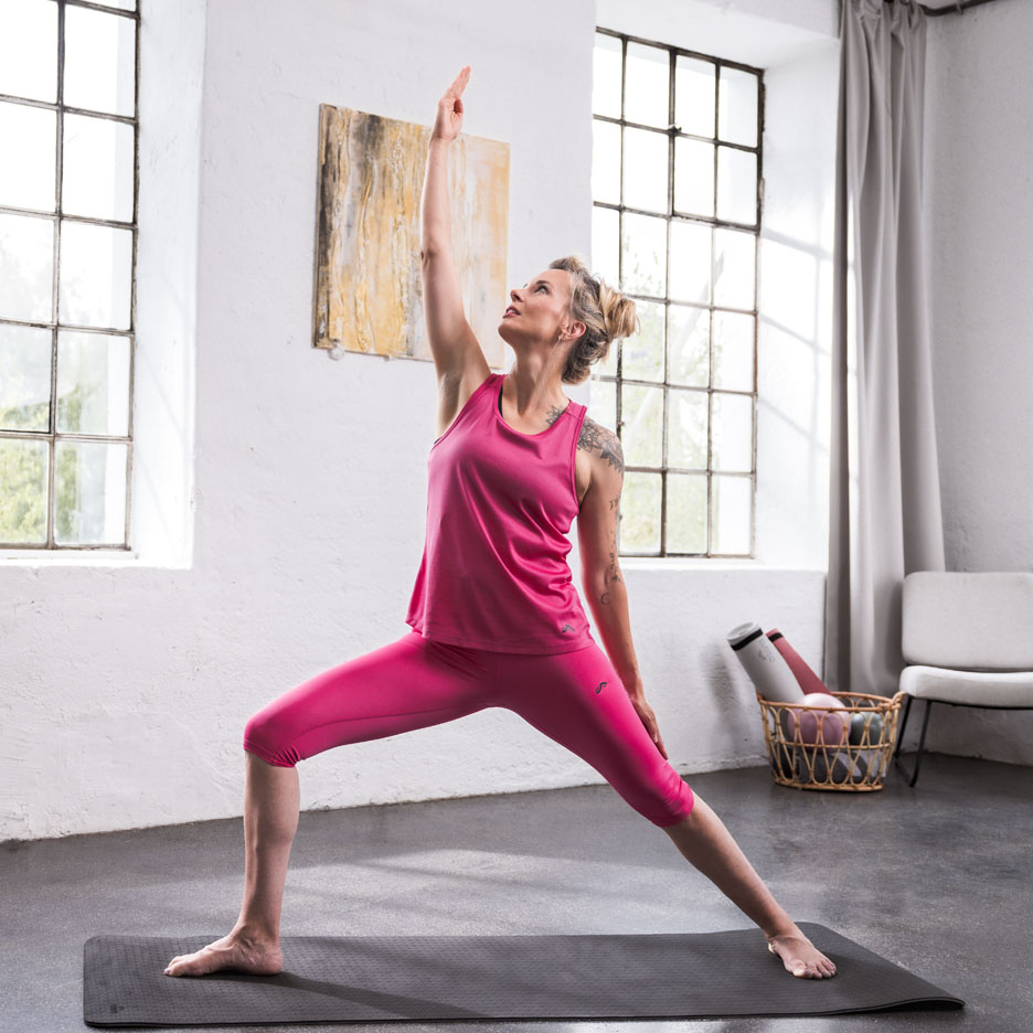 Femme faisant du yoga vêtue de vêtements de sport roses dans une pièce lumineuse.