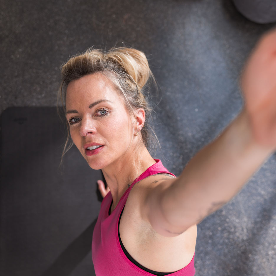 Une femme en débardeur de sport rose prend un selfie à la salle de sport.
