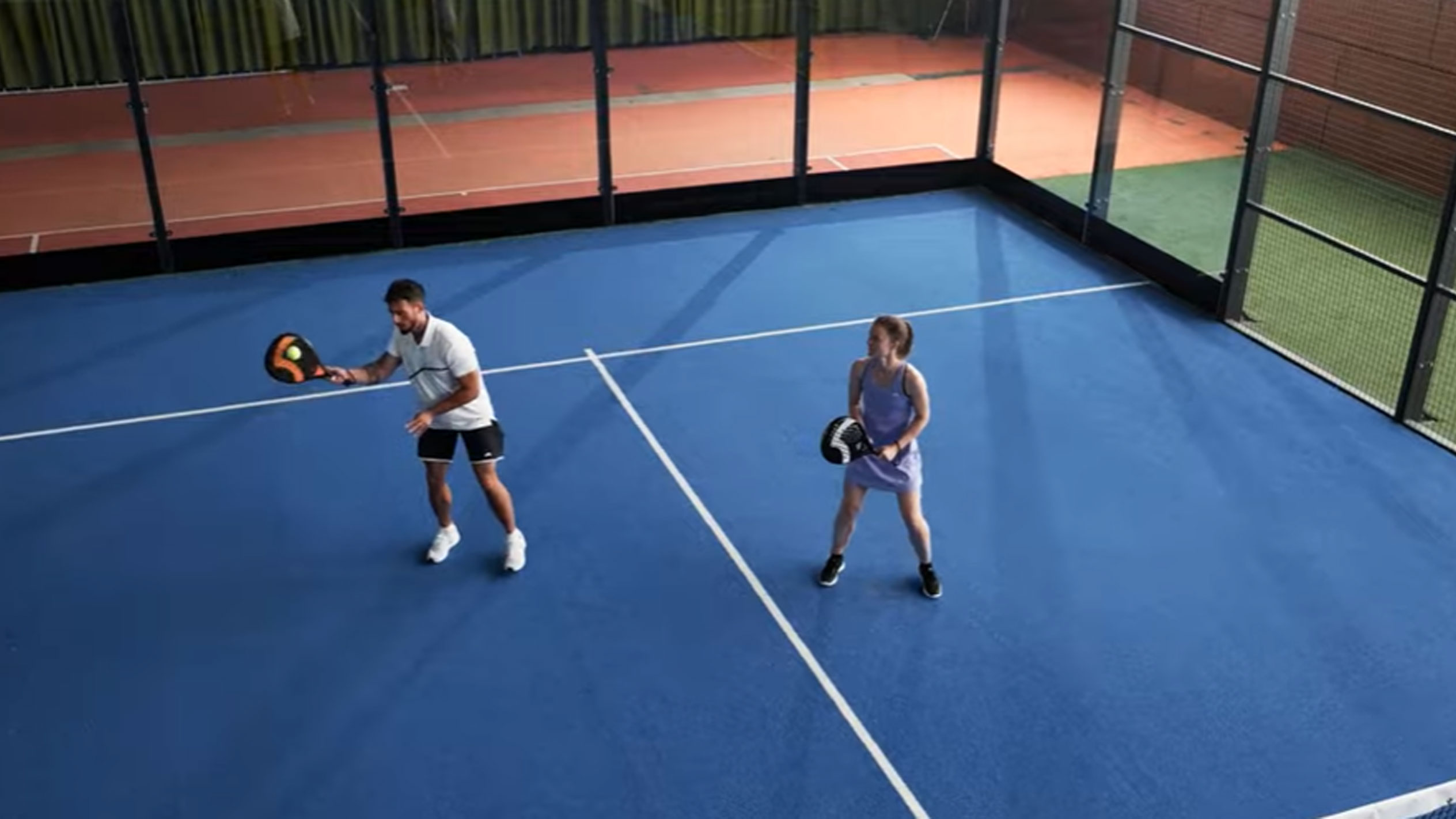 Uomo e donna giocano a padel su campo blu con racchette e palla
