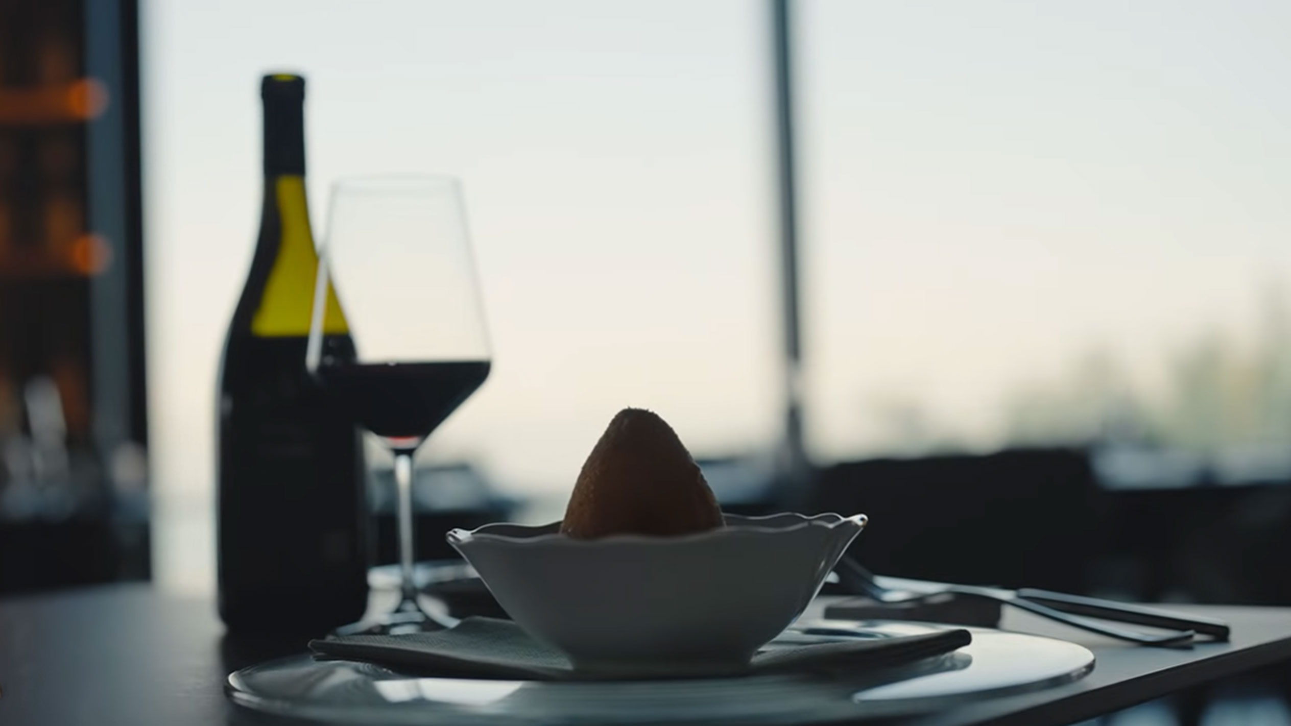 Une bouteille de vin rouge et un verre à côté d'un arancino dans un bol sur une table.