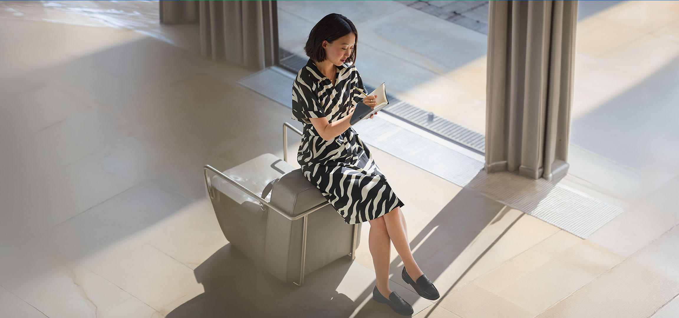 Femme en robe imprimé zèbre, assise sur une chaise, écrivant dans un carnet.