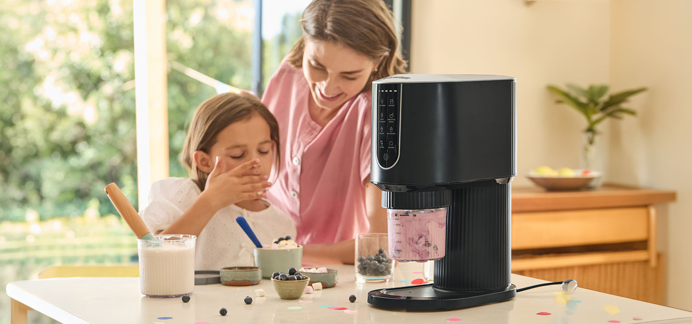 Frau und Mädchen bereiten Desserts mit einer Eismaschine zu, umgeben von Blaubeeren.