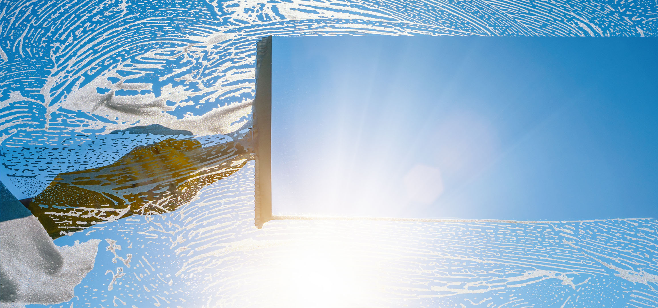 Pulizia finestre con schiuma di sapone su cielo blu.