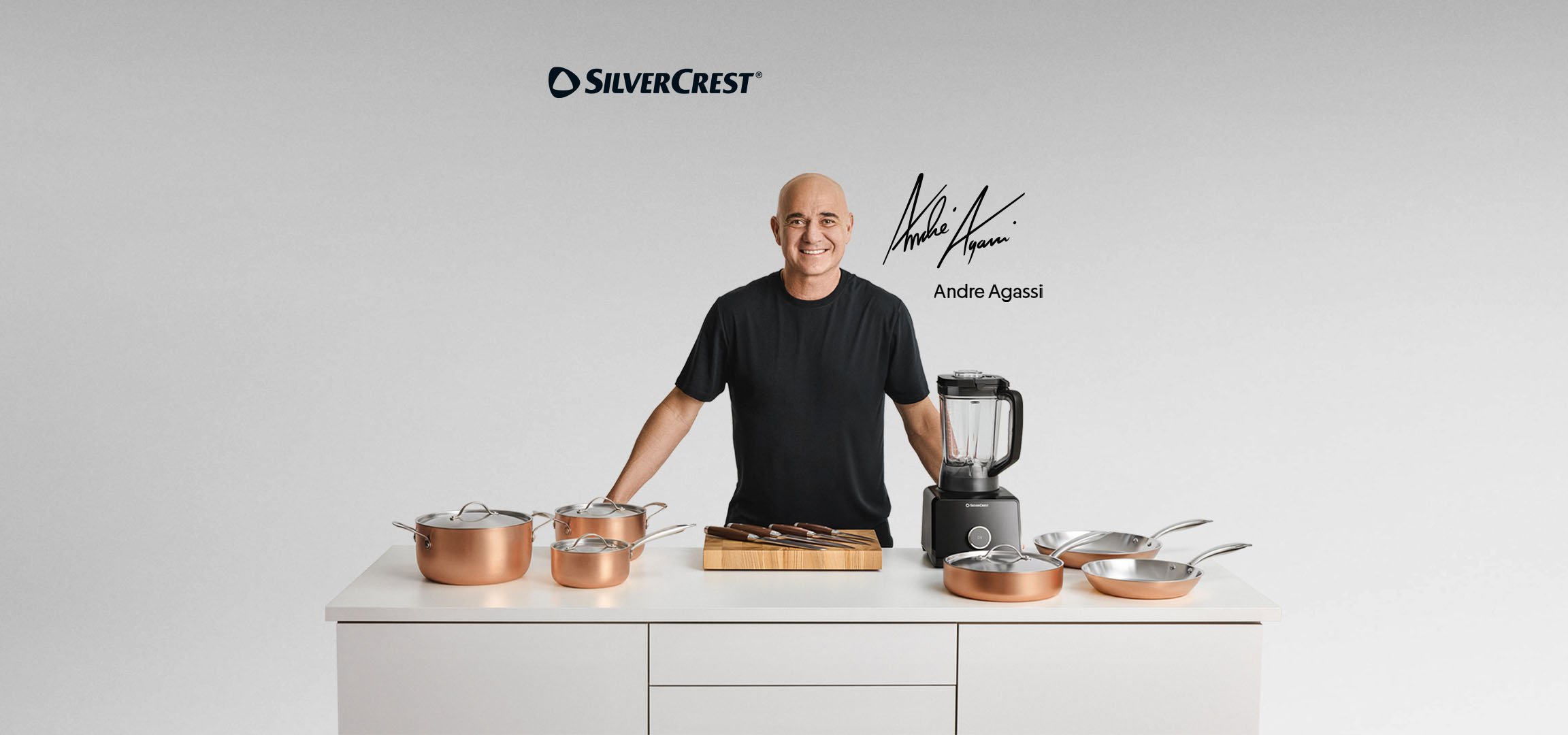 Andre Agassi mit einem Set kupferfarbener Töpfe, einem Mixer und einem Messerblock.