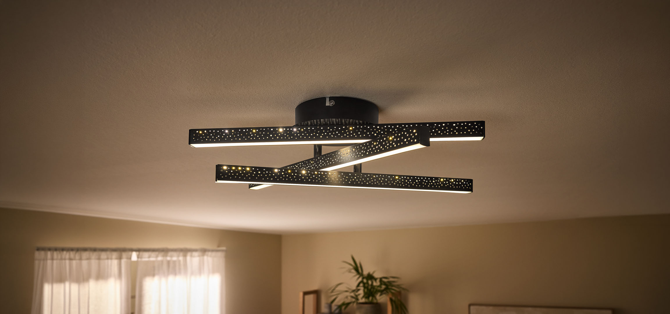 Moderne LED-Deckenleuchte mit schwarzen, perforierten Stäben und warmem Licht.