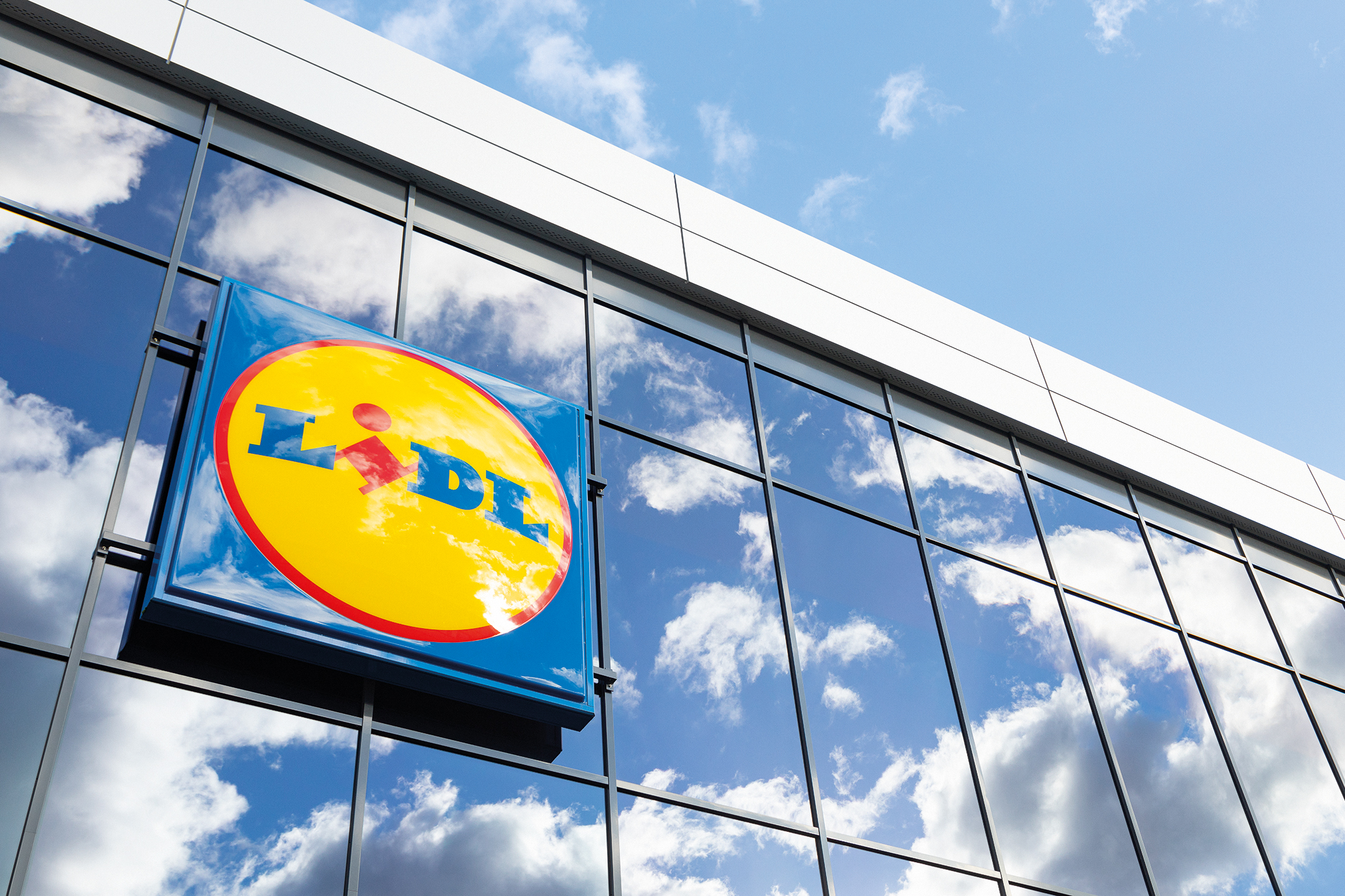 Enseigne Lidl sur une façade vitrée, avec le ciel et les nuages reflétés.