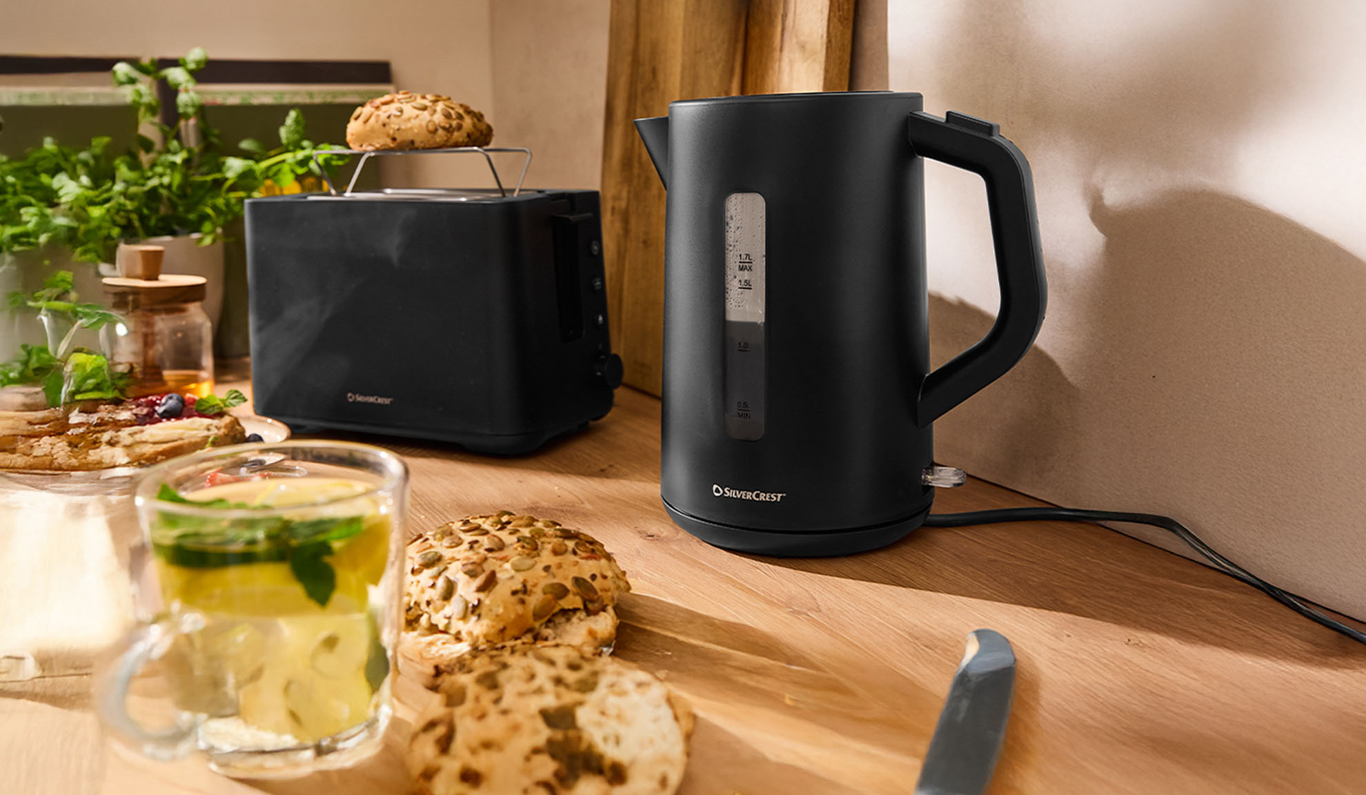 Bollitore e tostapane neri SilverCrest su un tavolo di legno con colazione.