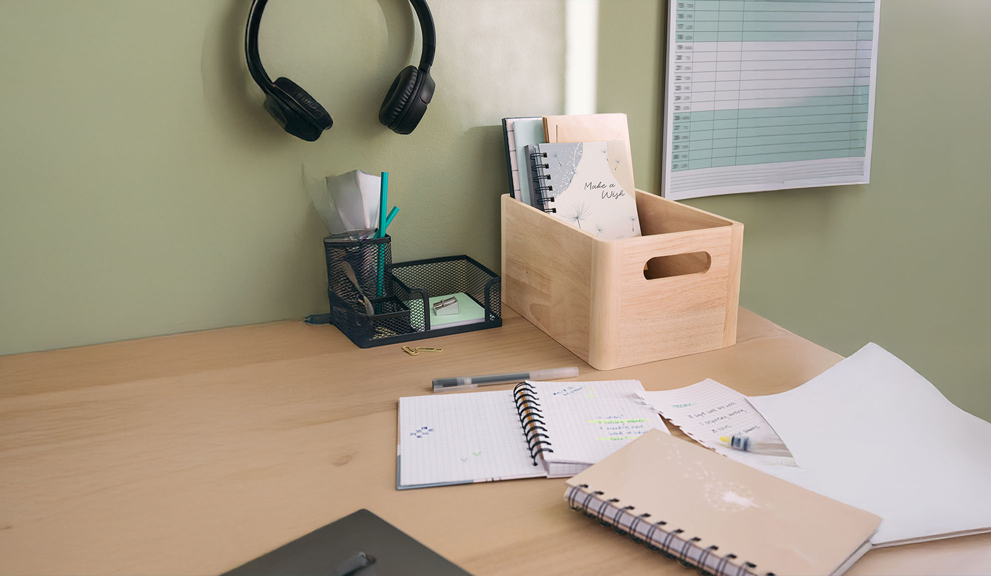 Bureau avec casque, organiseur en maille, boîte en bois avec cahiers et fournitures de bureau.