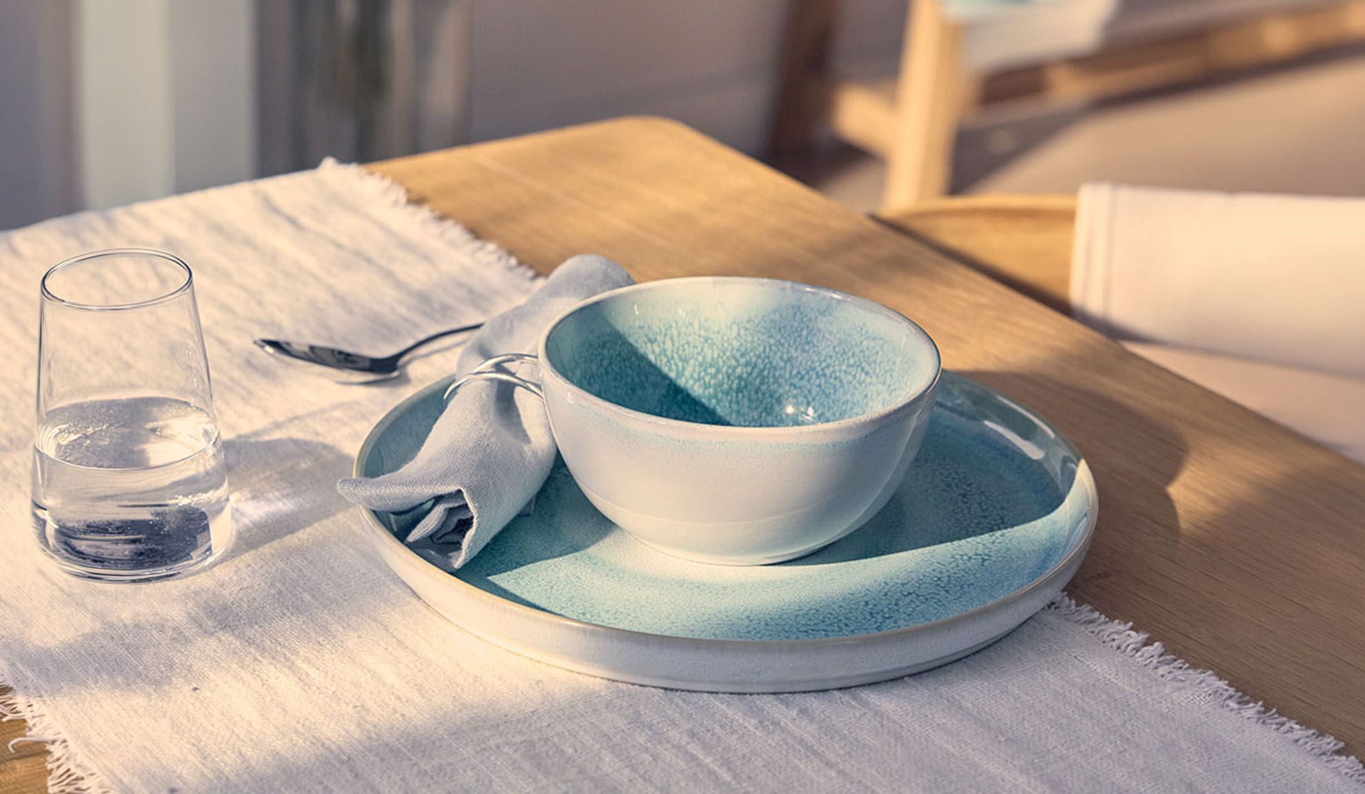 Table dressée avec un bol bleu, une assiette, un verre d'eau et une serviette sur une table en bois.