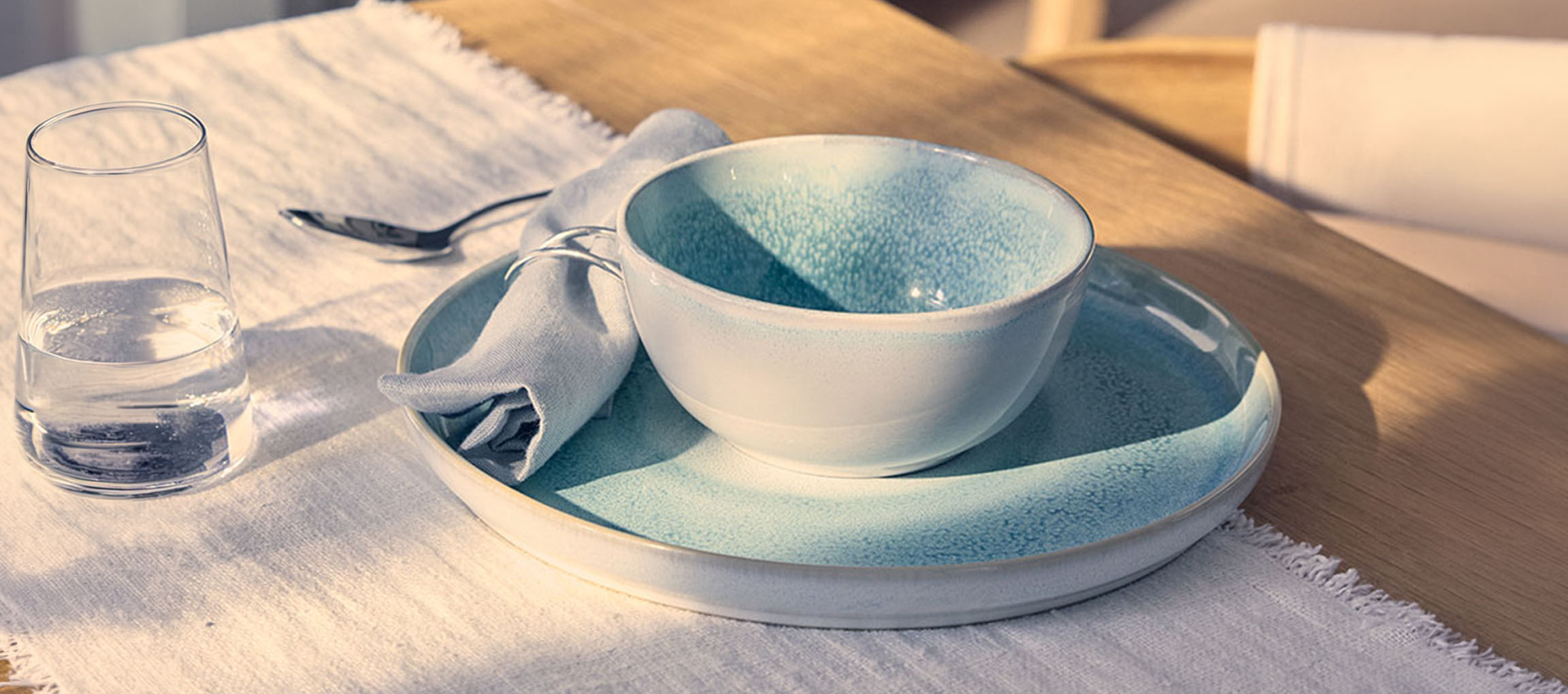 Table dressée avec un bol et une assiette en céramique bleue, un verre d'eau et une serviette.