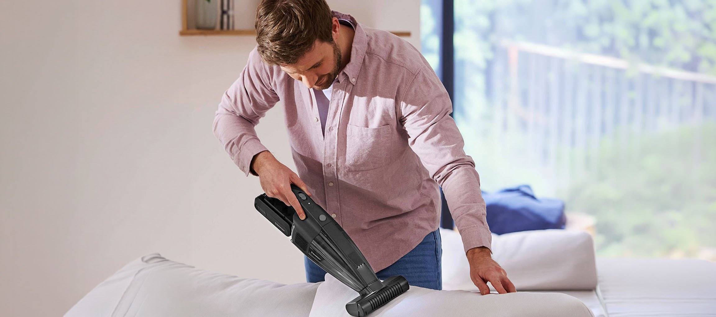 Uomo che pulisce un divano con un aspirapolvere portatile.