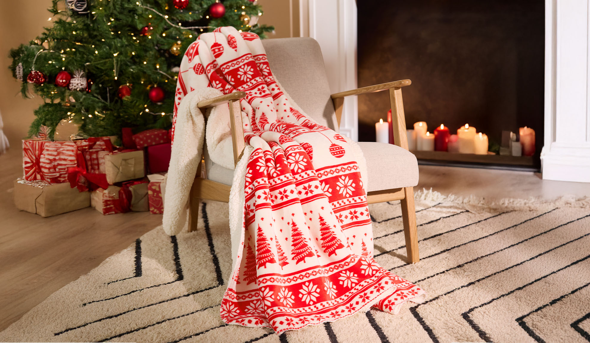 Plaid de Noël rouge et blanc sur un fauteuil à côté d'un sapin de Noël illuminé et de cadeaux.
