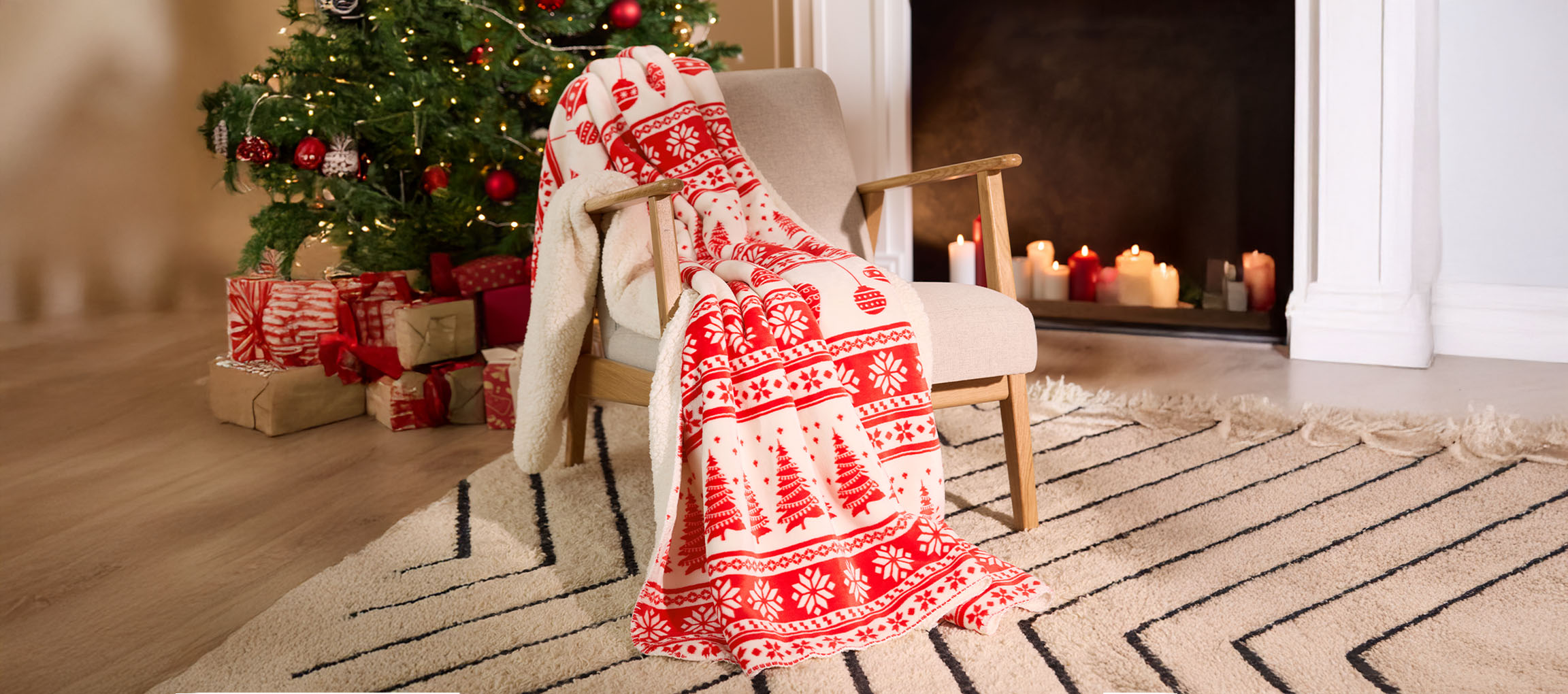 Plaid de Noël sur une chaise, avec sapin décoré et cadeaux dans une pièce chaleureuse.