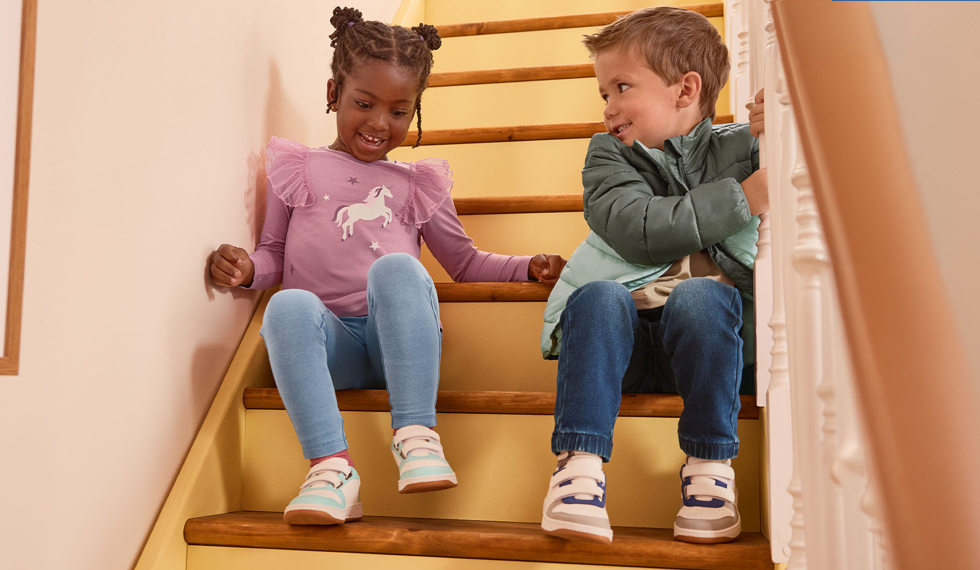 Deux enfants en vêtements décontractés et baskets assis sur des escaliers en bois, se souriant.