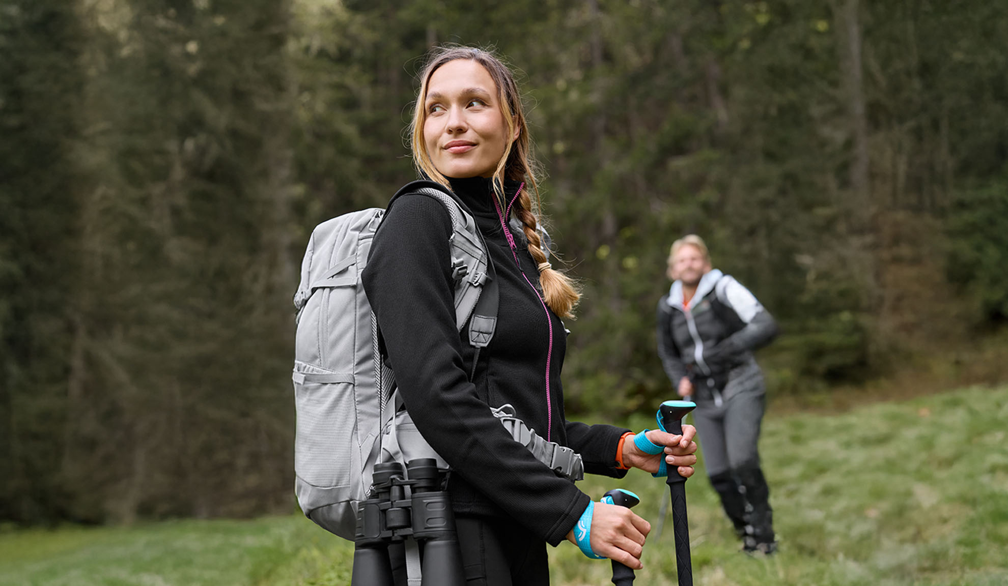 Frau mit Wanderrucksack und Trekkingstöcken, Mann im Hintergrund.