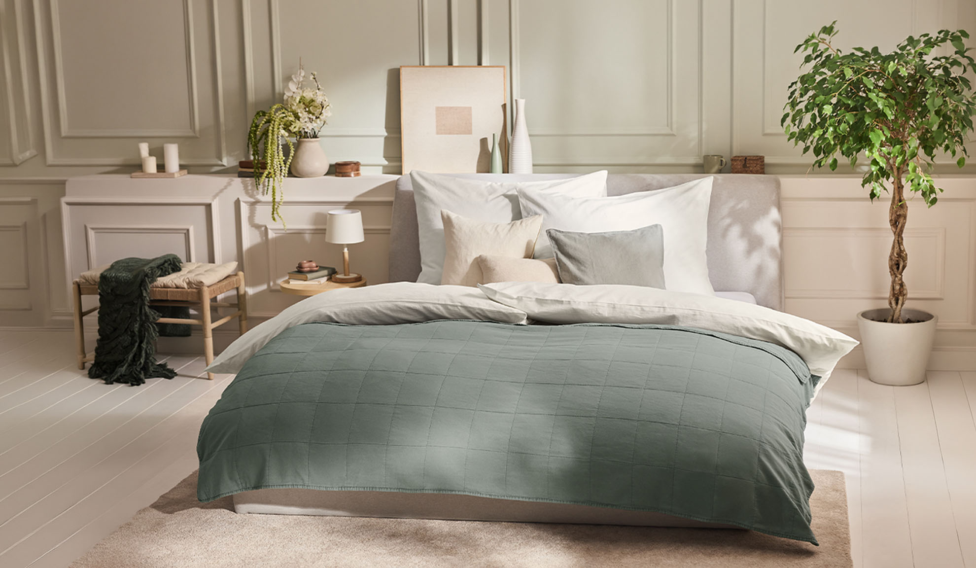 Chambre à coucher avec un lit, une housse de couette verte, des oreillers blancs et une plante