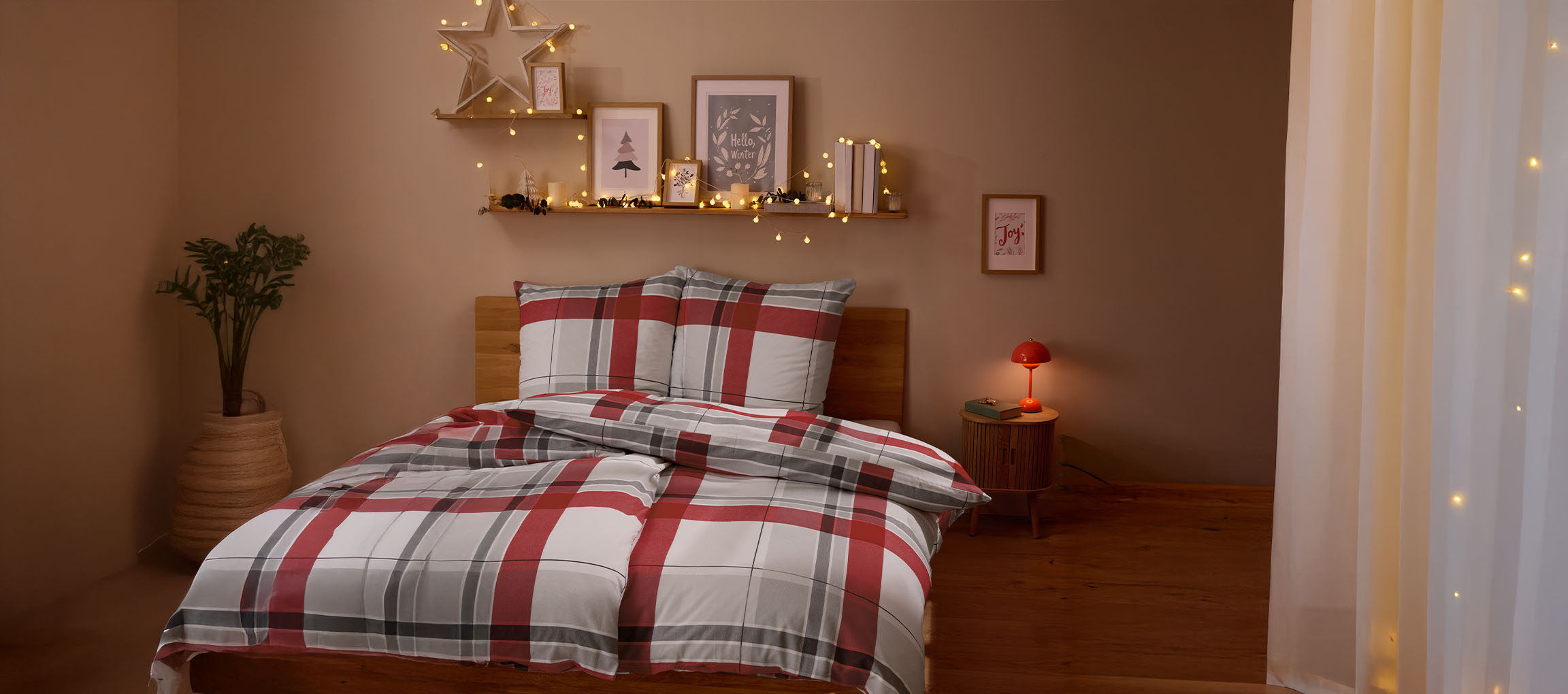 Chambre douillette avec parure de lit à carreaux rouges et gris, décorations de Noël et guirlandes lumineuses.