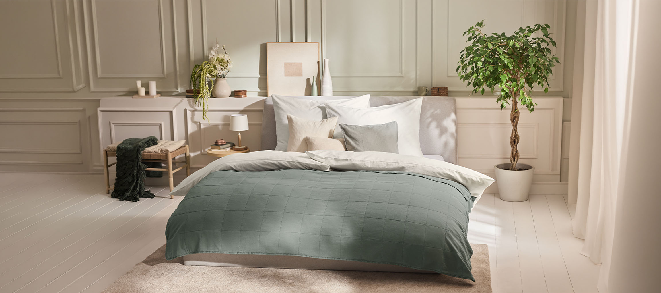 Chambre à coucher avec un lit, une couette verte, des oreillers, une table de chevet et une plante.
