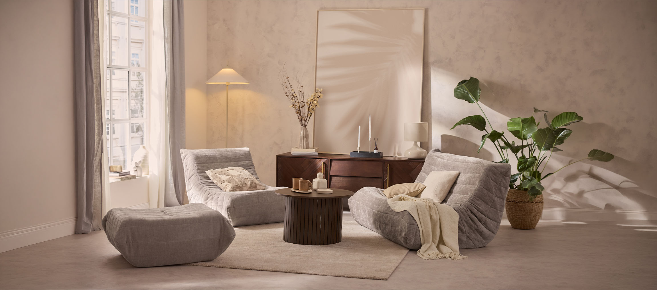 Accogliente soggiorno con due poltrone lounge grigie, un pouf e un tavolo in legno.