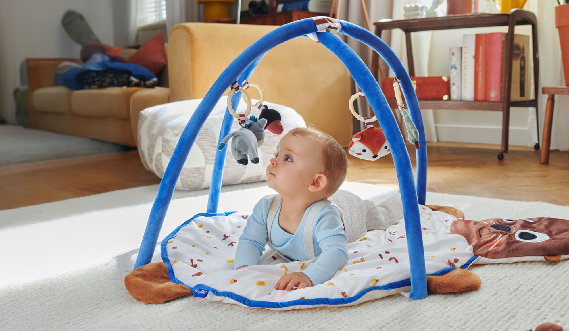 Ein Baby spielt auf einer Tiny Love Spielmatte mit Tier-Bogen.