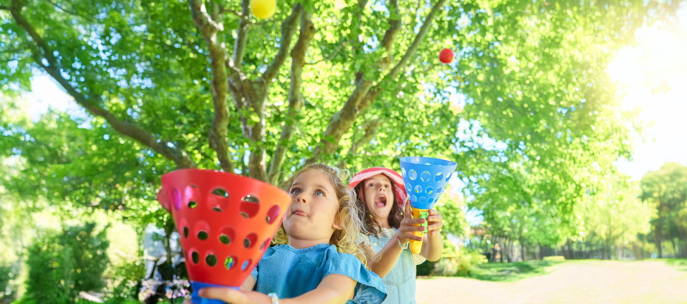 Zwei Mädchen spielen im sonnigen Park mit Wurfspielzeug.