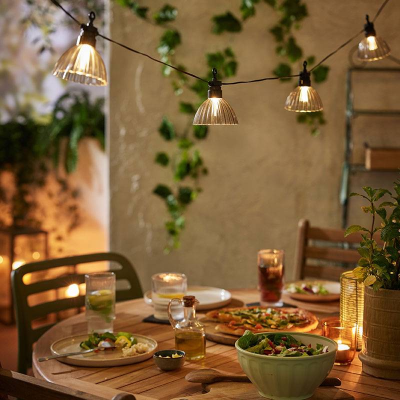 Guirlandes lumineuses extérieures avec des lumières chaudes au-dessus d'une table en bois avec de la nourriture.