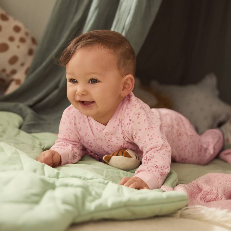 Bébé en pyjama rose à étoiles, allongé sur une couverture verte avec une peluche.