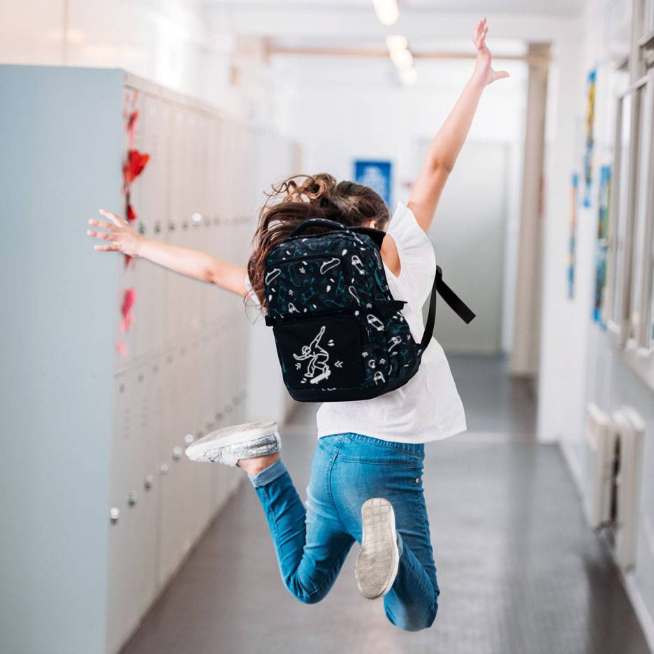 Enfant avec sac à dos sautant dans un couloir d'école.