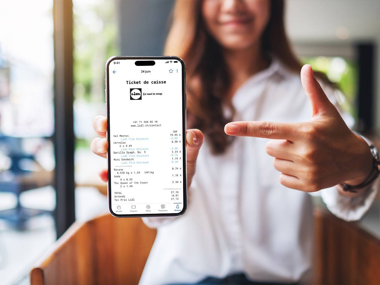 Une femme pointe du doigt un reçu numérique sur son smartphone, affichant des achats comme des bananes, des saucisses et des pâtes.