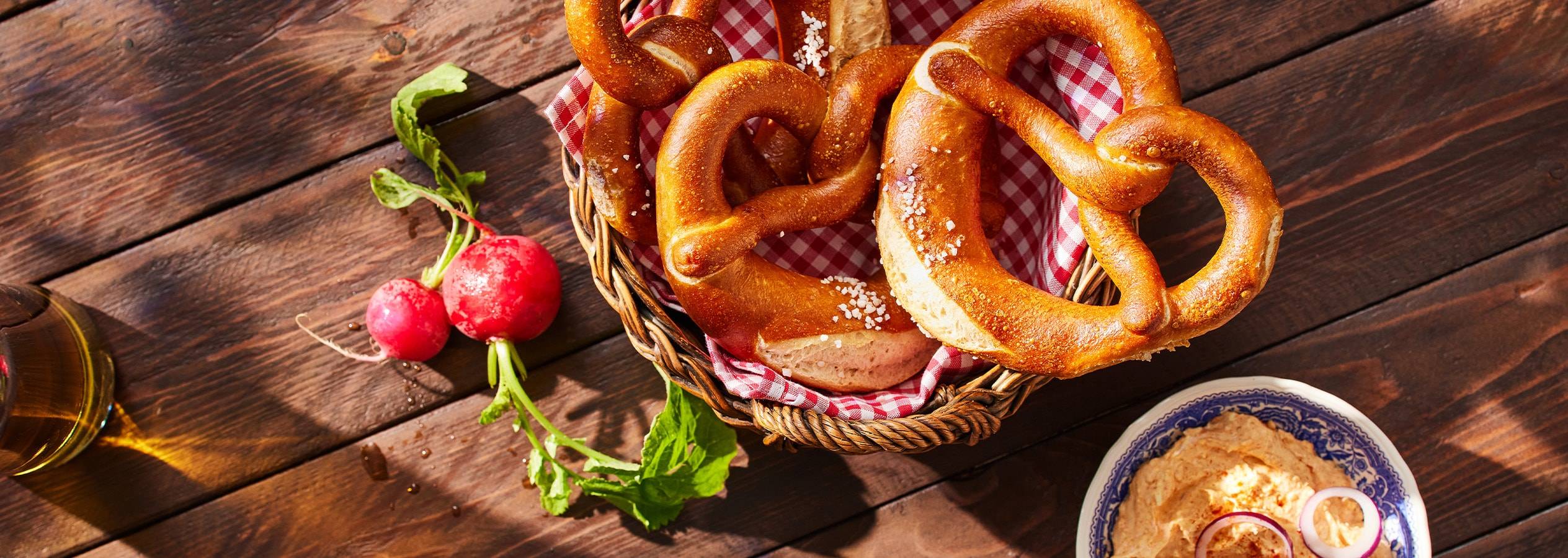 Brezeln in einem Korb mit Radieschen und Dip auf einem Holztisch.