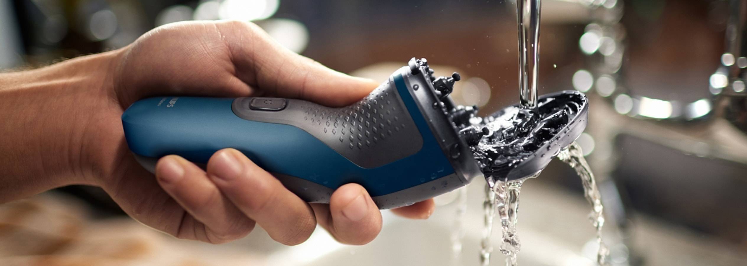 Un homme rince un rasoir électrique Philips sous l'eau courante.