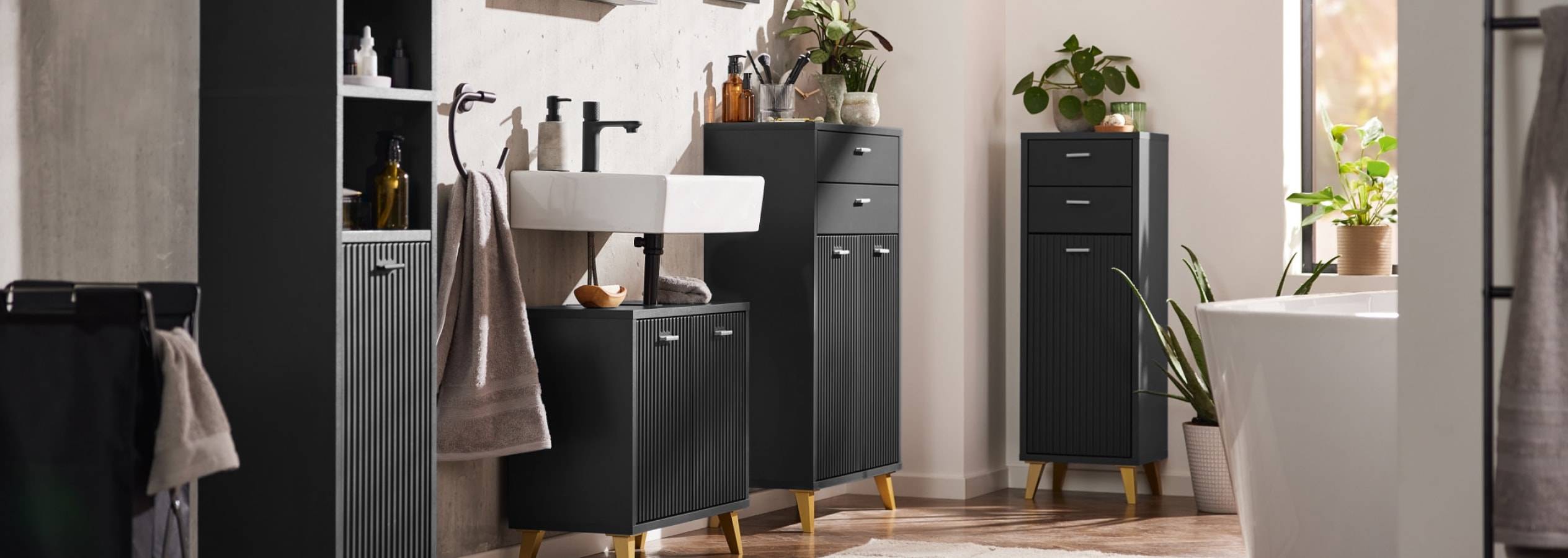 Schwarze Badmöbel mit weißem Waschbecken und grünen Pflanzen.