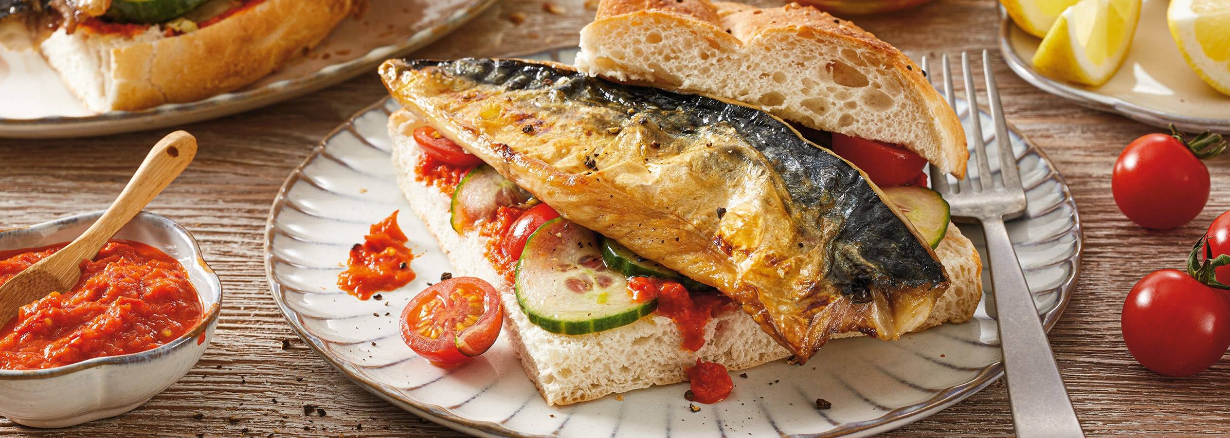 Un sandwich au maquereau, tomates et concombres, avec de la sauce et des citrons en arrière-plan.