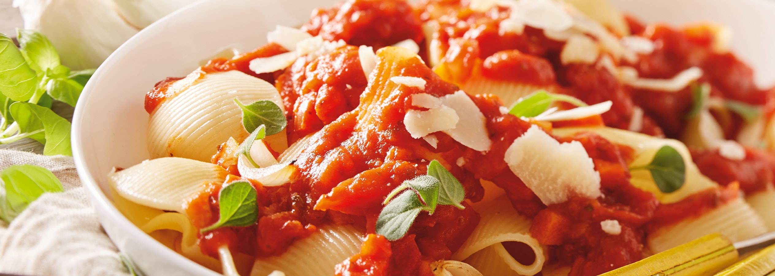 Eine Schüssel mit Muschelnudeln in Tomatensauce, garniert mit Käse und Kräutern.