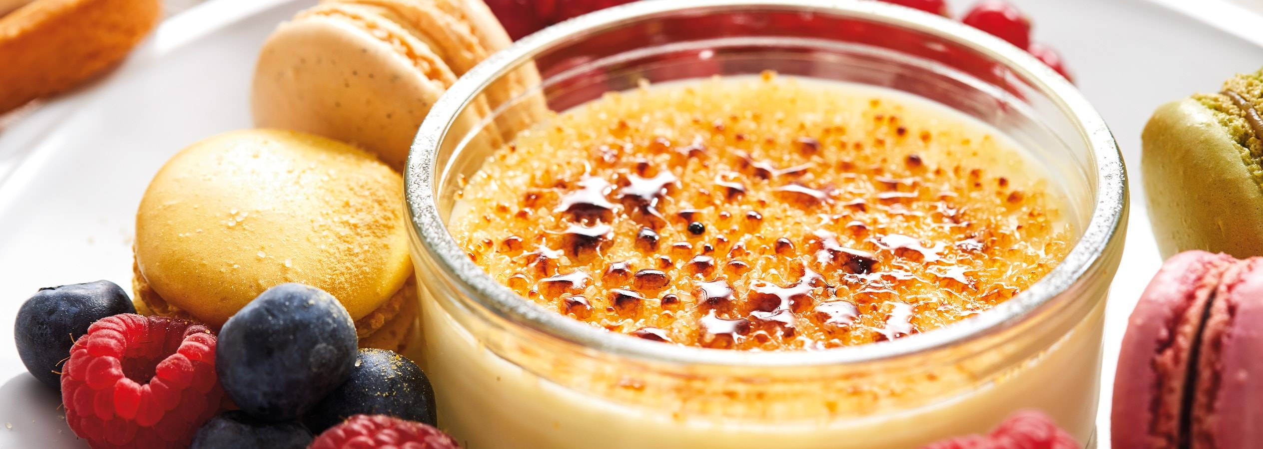 Crème brûlée mit Beeren und Macarons auf einem weißen Teller.