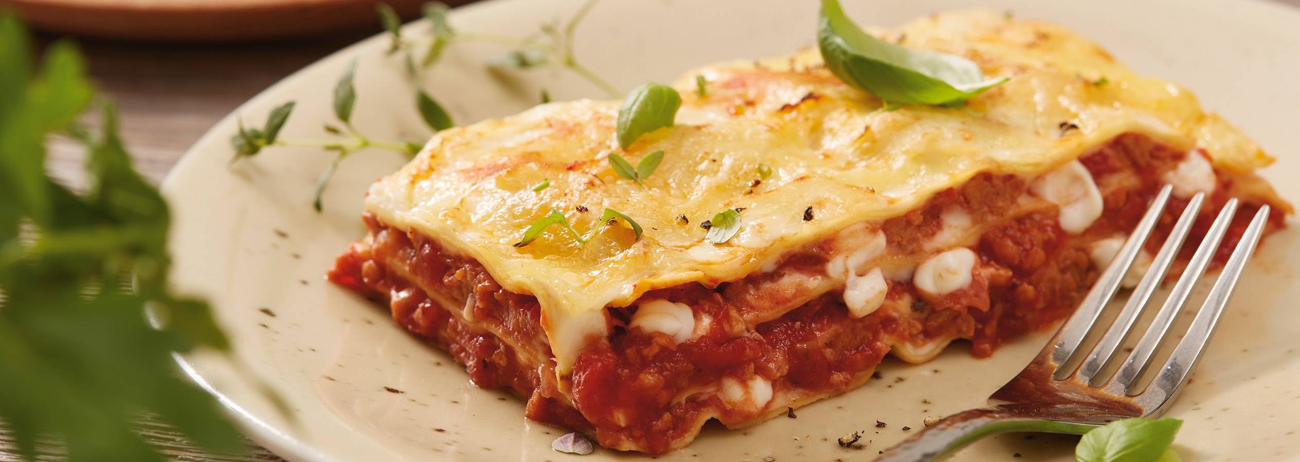 Ein Stück Lasagne auf einem Teller, garniert mit Basilikum.