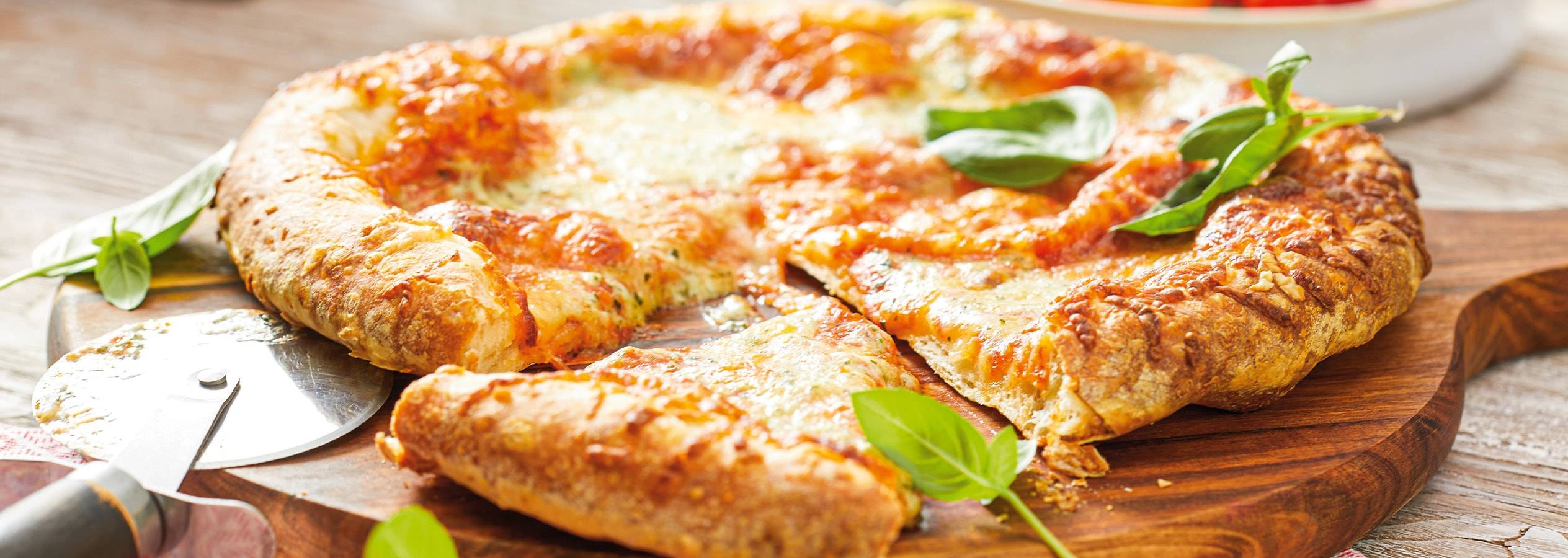 Selbstgemachte Pizza mit Käse und Basilikum, auf einem Holzbrett serviert.
