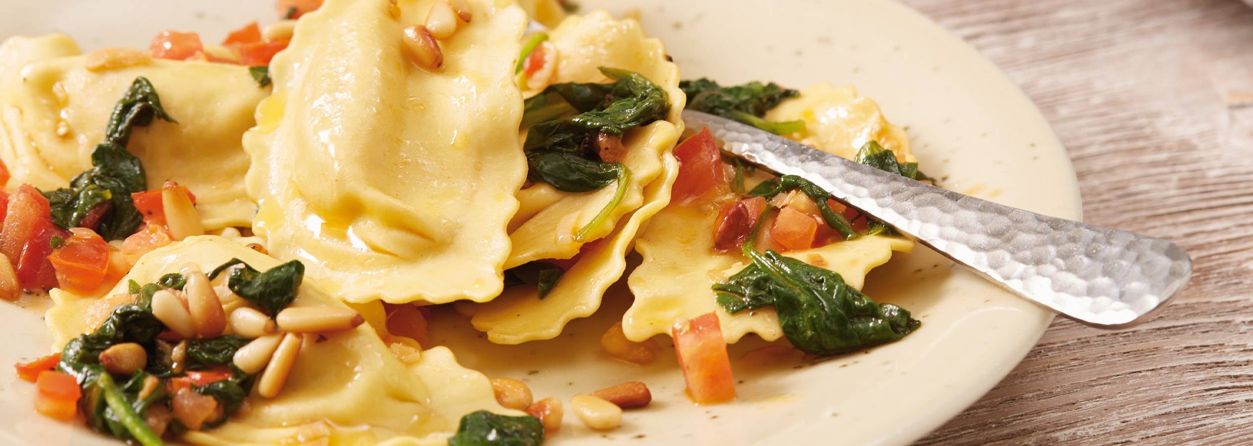 Ravioli con spinaci, pomodori e pinoli su un piatto con una forchetta.